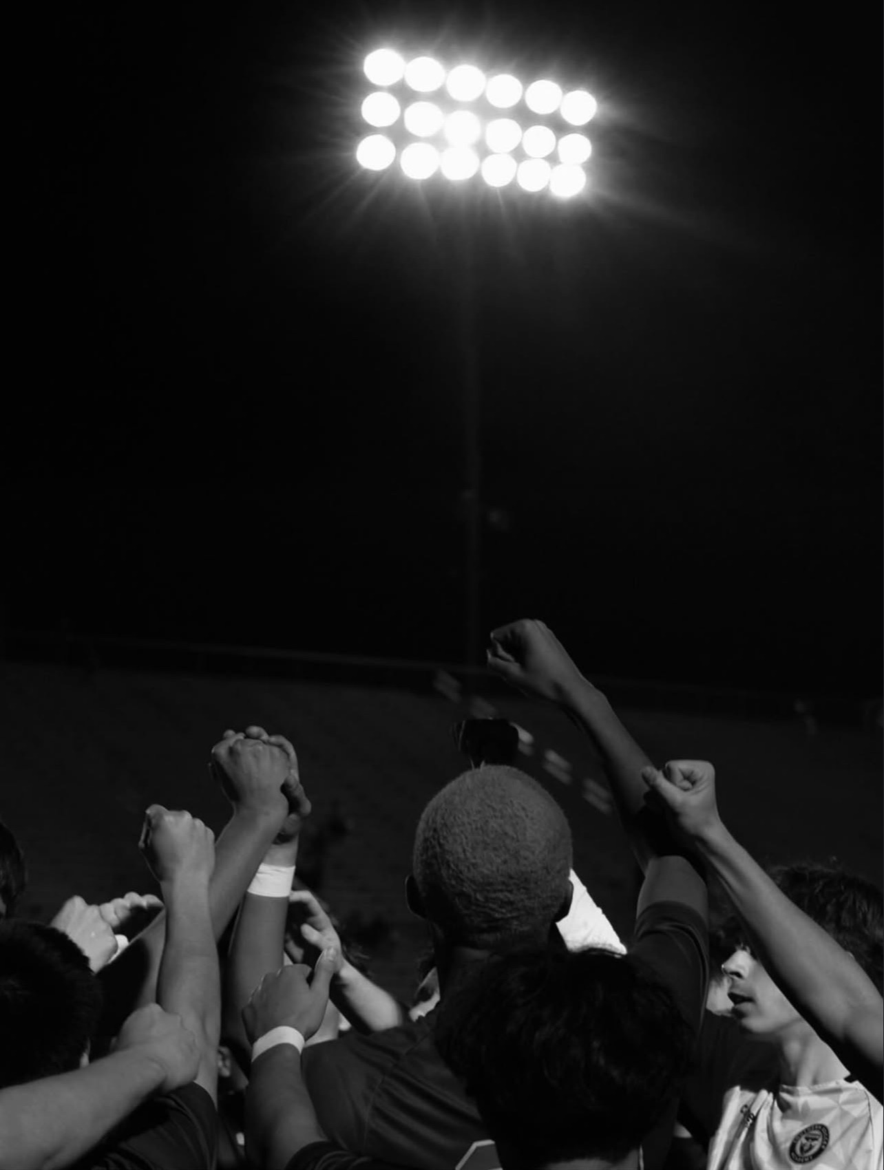 Teammates raising their hands beneath stadium lights