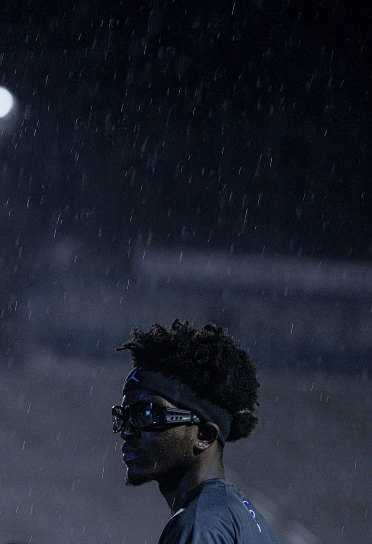 Athlete standing in the rain beneath stadium lights