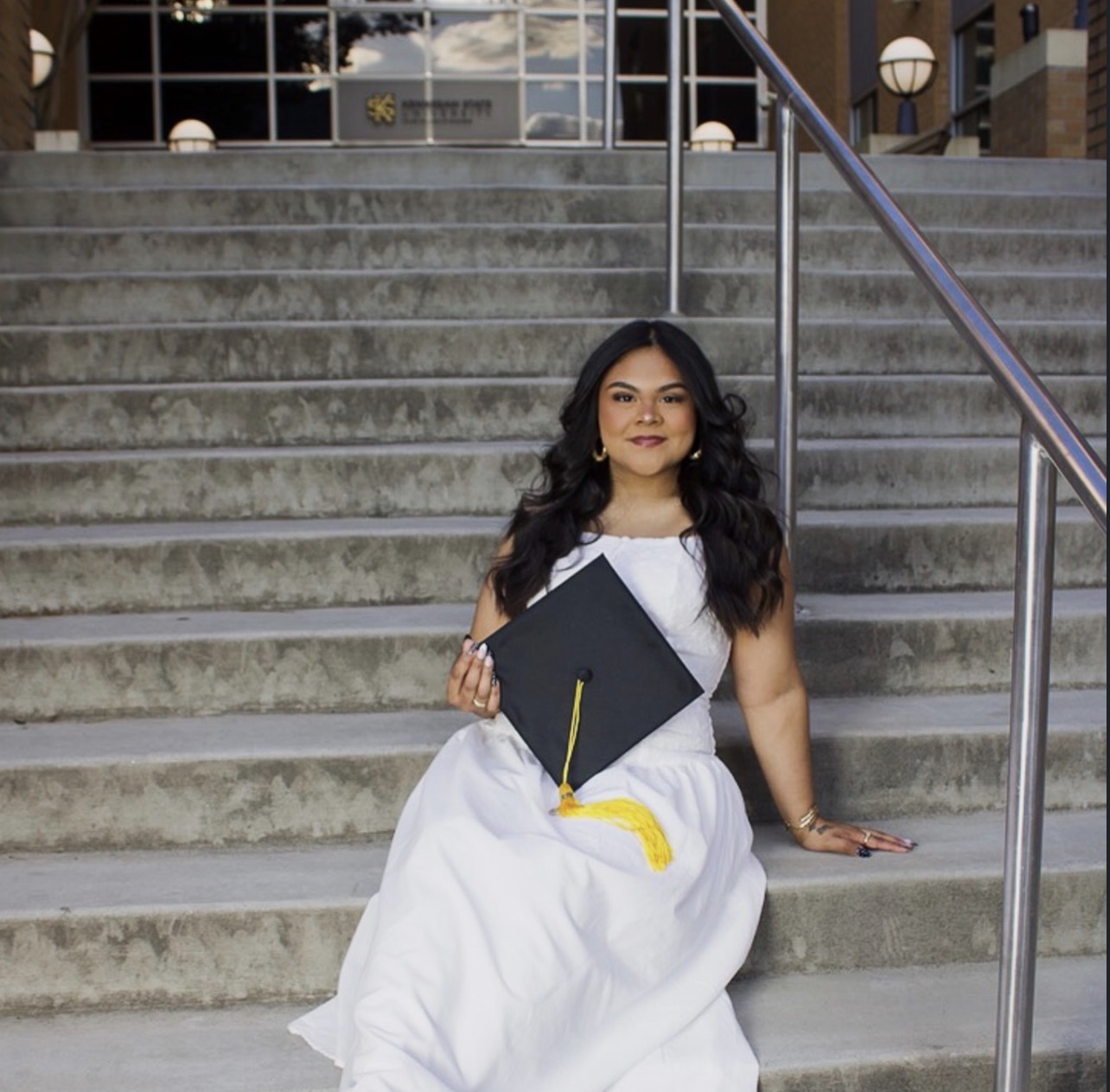 Graduate seated on university steps holding her graduation cap