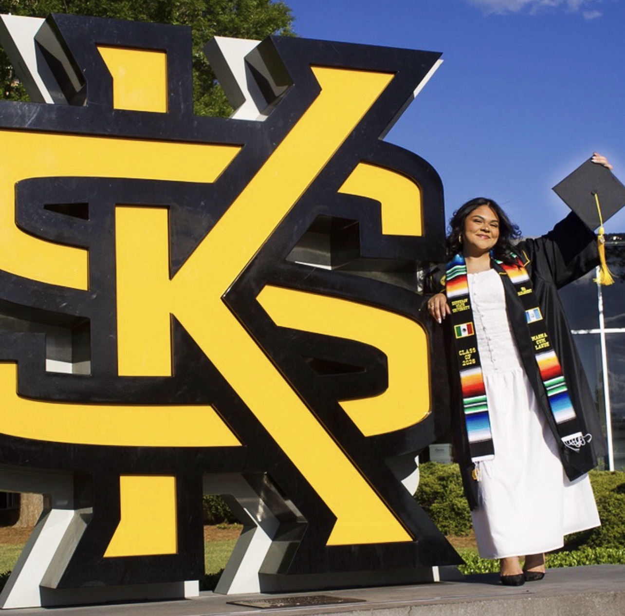 Graduate posing beside the Kennesaw State University sculpture