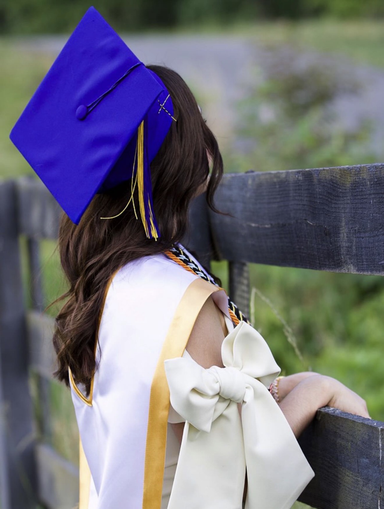 Graduate in cap and stole seated beside a rustic fence